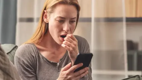 Getty Images Woman looking at her phone with a shocked expression on her face.